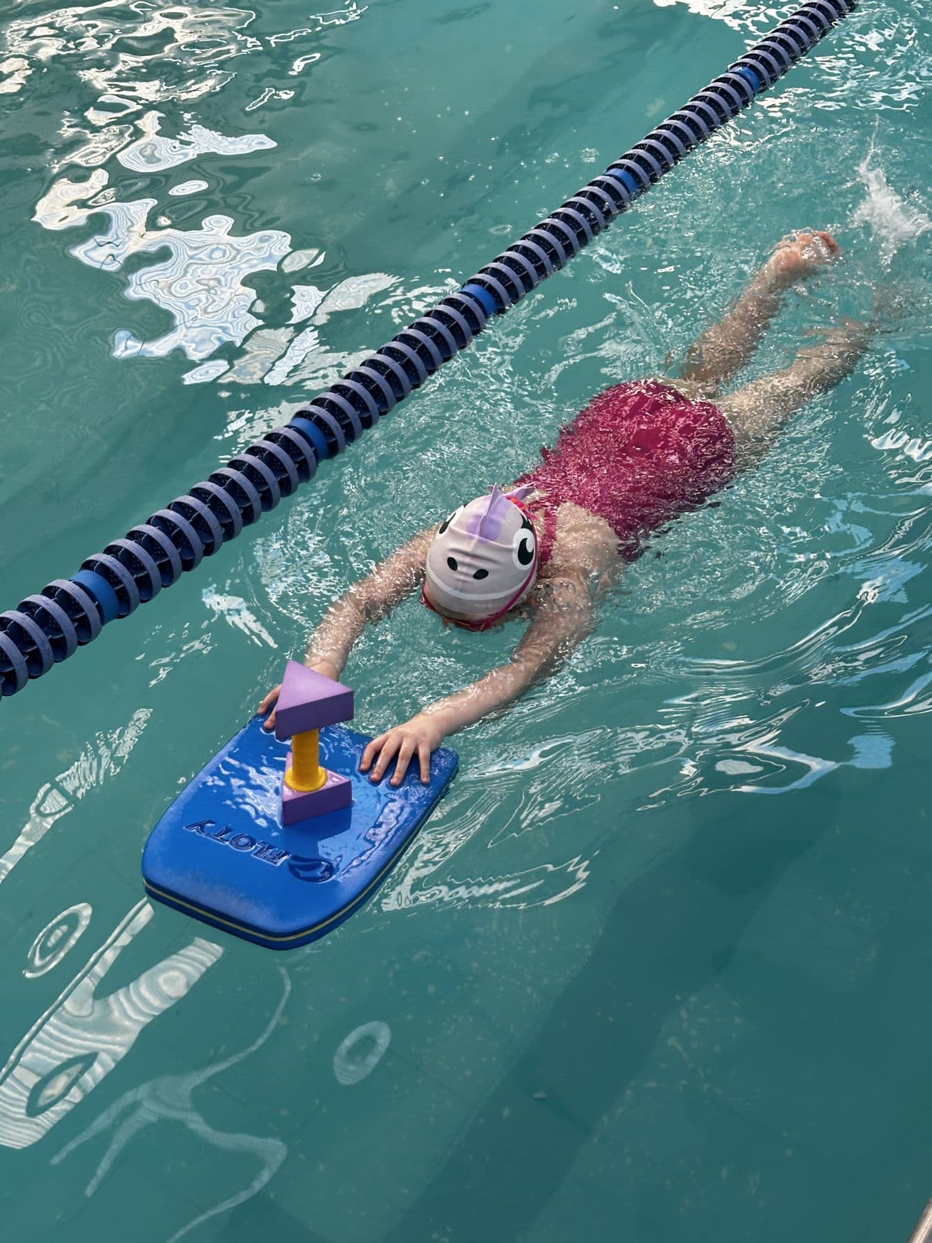 Criança nadando sozinha na piscina com uma prancha