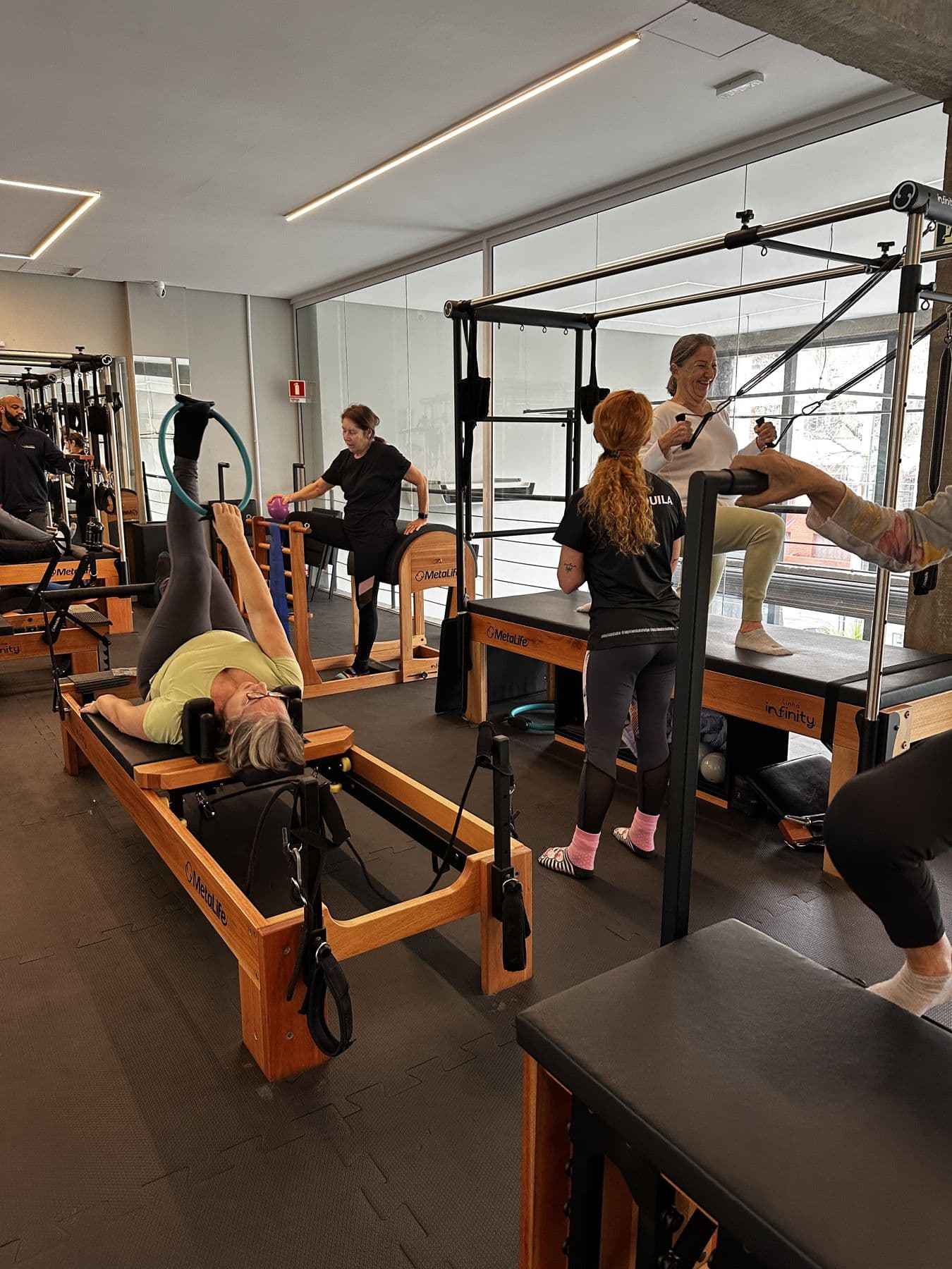 Alunas fazendo pilates nos aparelhos, com a instrutora acompanhando